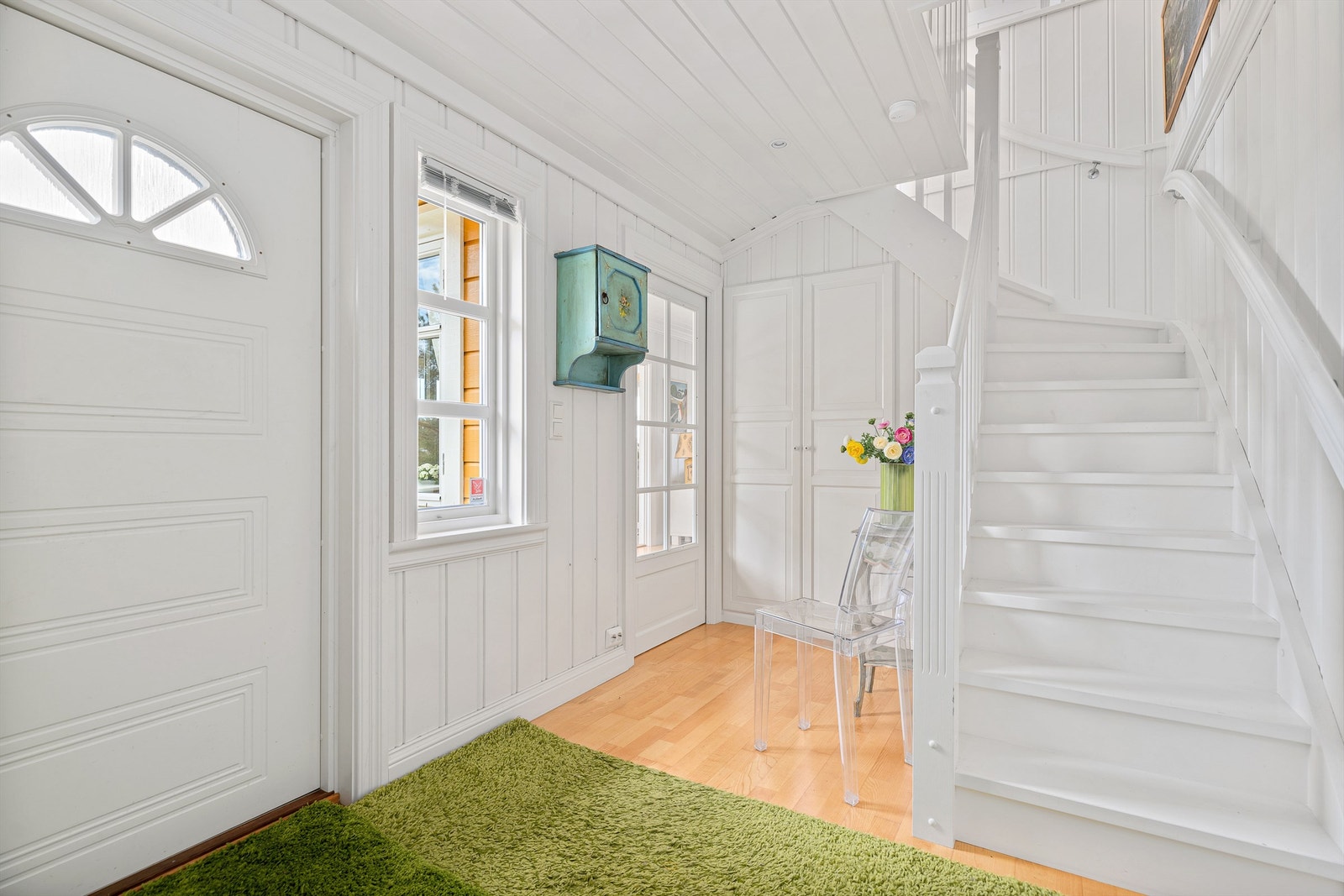 Lys og innbydende entré med parkett på gulvet og svingtrapp opp til loftsetasjen Galleribilde