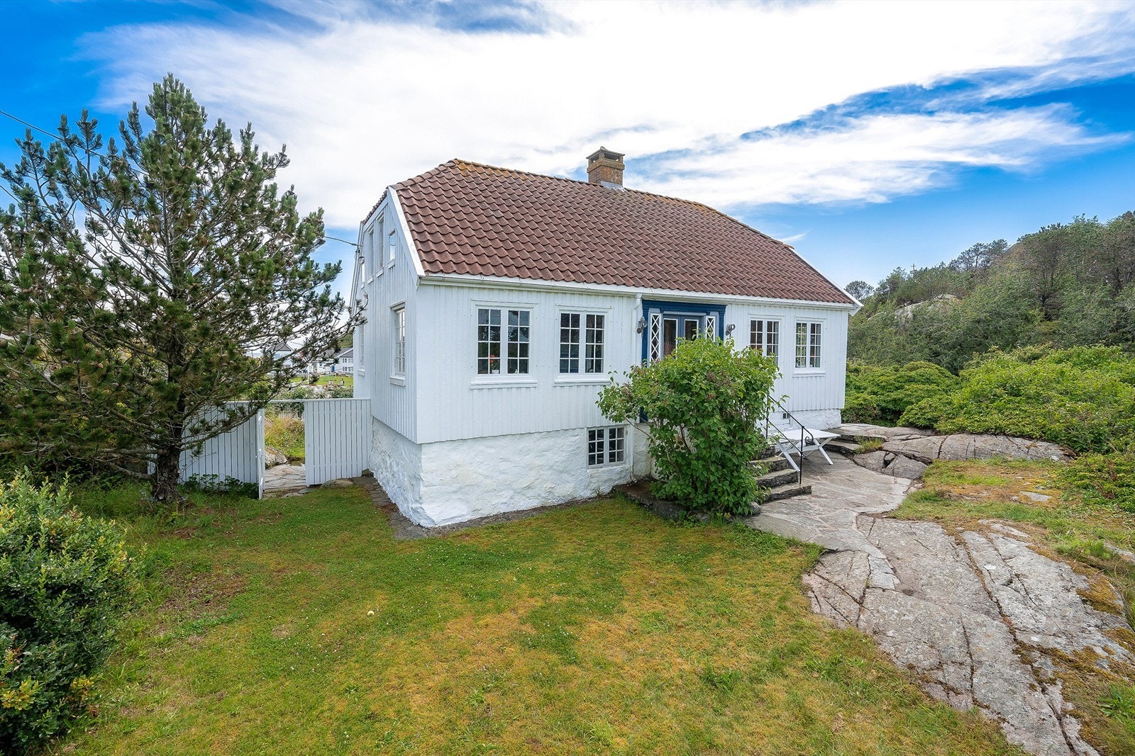 Huset er omkranset av mye grøntarealer og beplantning som busker og trær. Galleribilde