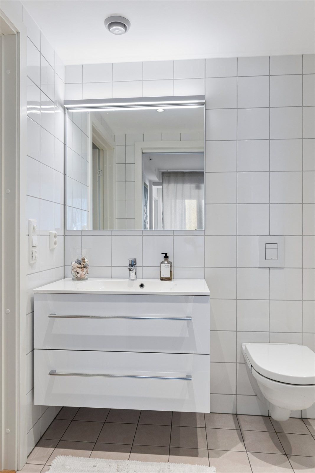 Baderomsinnredning med heldekkende servant, vegghengt toalett og downlights i himlingen. Galleribilde