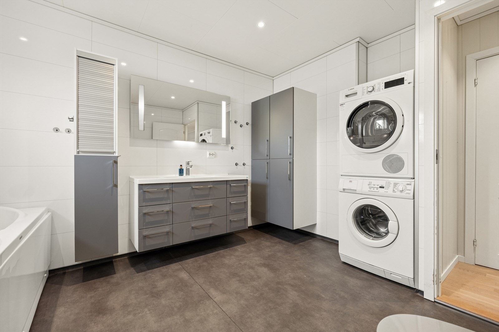 Rommet er innredet med en baderomsinnredning med nedfelt servant, et dusjhjørne med glassvegger, badekar og et vegghengt toalett samt opplegg for vaskemaskin. Galleribilde