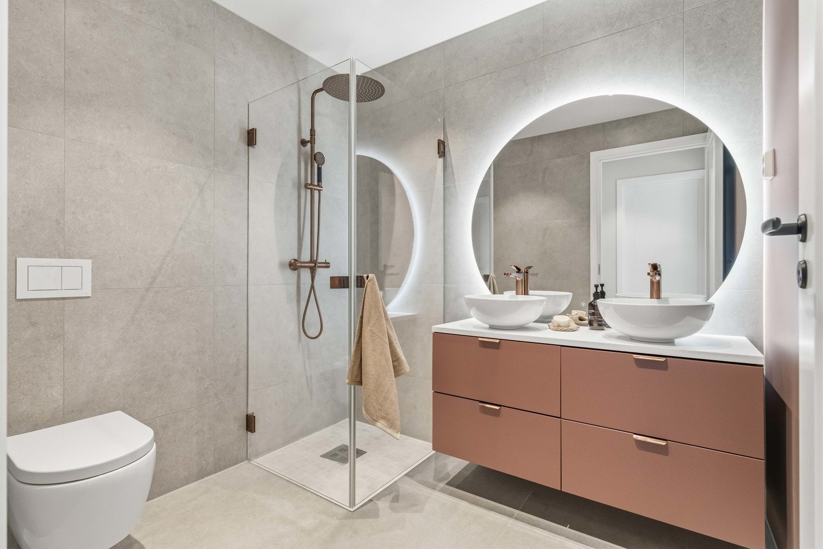 Stilrent og moderne familiebad med flislagte overflater, varmekabler i gulv og servant med tilhørende innredning. Badet har et ryddig og gjennomført uttrykk med god oppbevaringsplass. Galleribilde