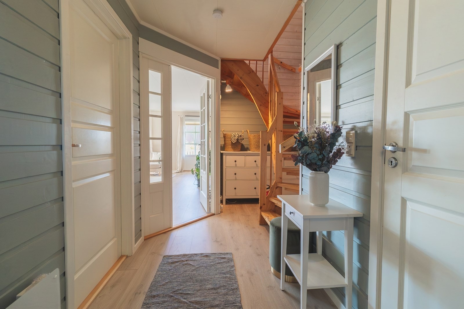 Gangen leder mot trapp til 2. etasje og inn til både stue og kjøkken. Fra gangen får du en naturlig og oversiktlig forbindelse til boligens hovedrom Galleribilde