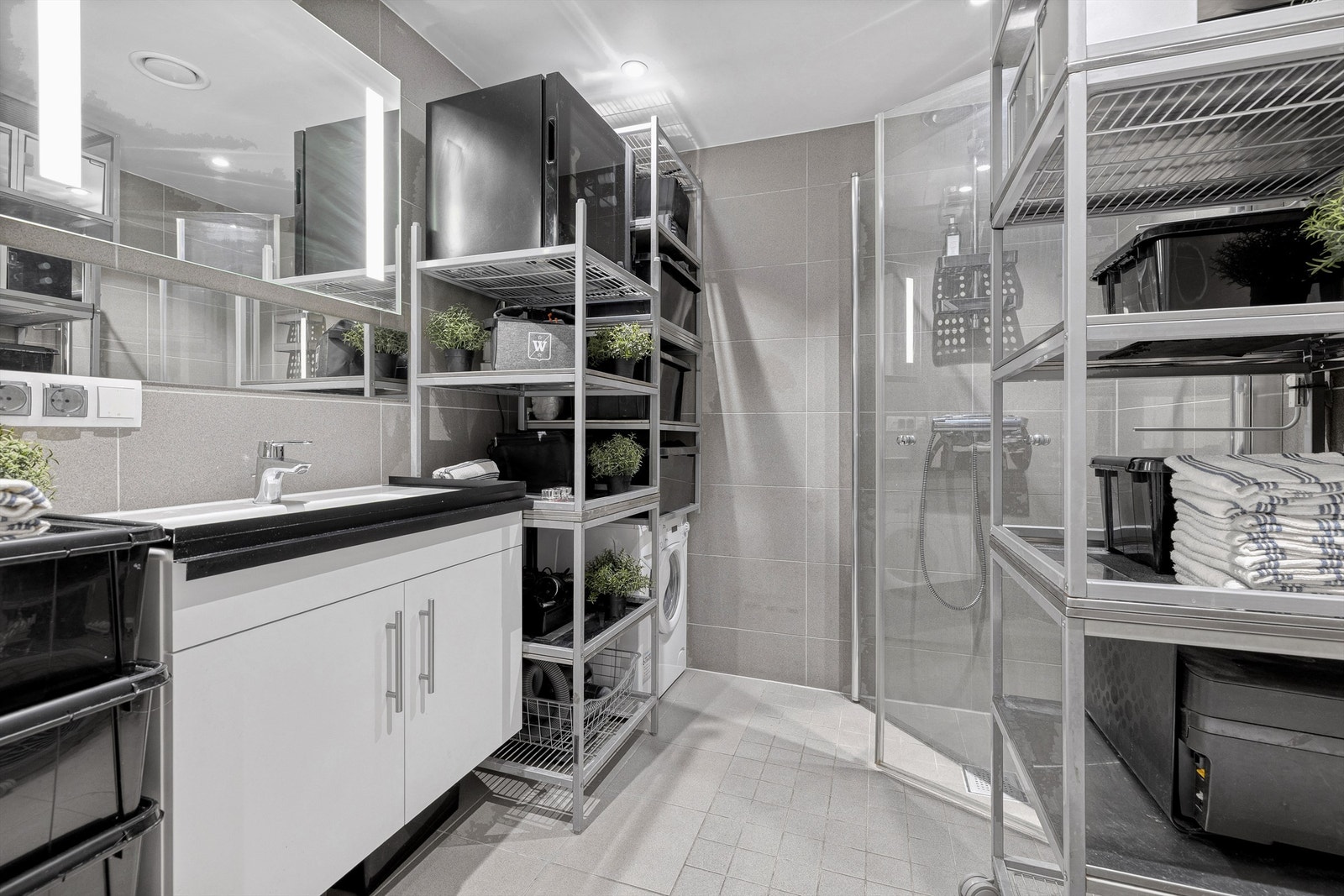 Moderne, prefabrikkert baderom fra byggeår med servant, speil med belysning og opplegg for vaskemaskin. Galleribilde