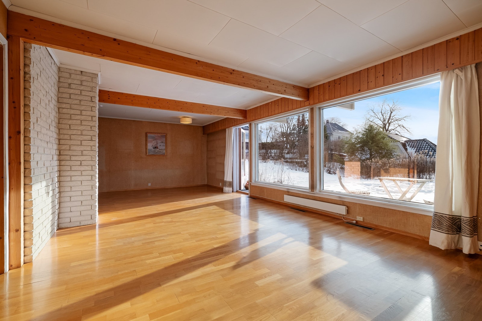 Boligens oppholdsrom fremstår åpent, luftig og lyst med store vinduer og mye naturlig lys ettersom rommet vender mot syd. Galleribilde