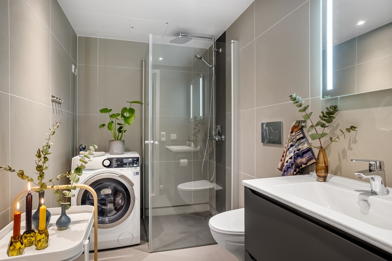 Delikat, flislagt bad med vegghengt toalett og dusjhjørne med dører i herdet glass. Galleribilde