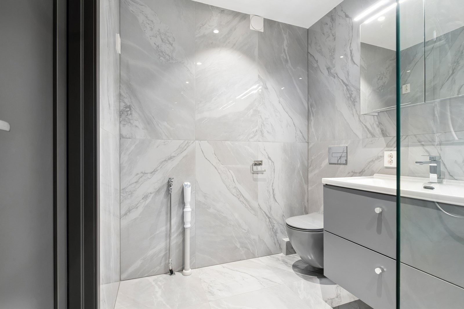 Rommet er innredet med benk og heldekkende porselensvask, innebygget vegghengt klosett, dusjhjørne med glassvegger og opplegg for vaskemaskin. Galleribilde