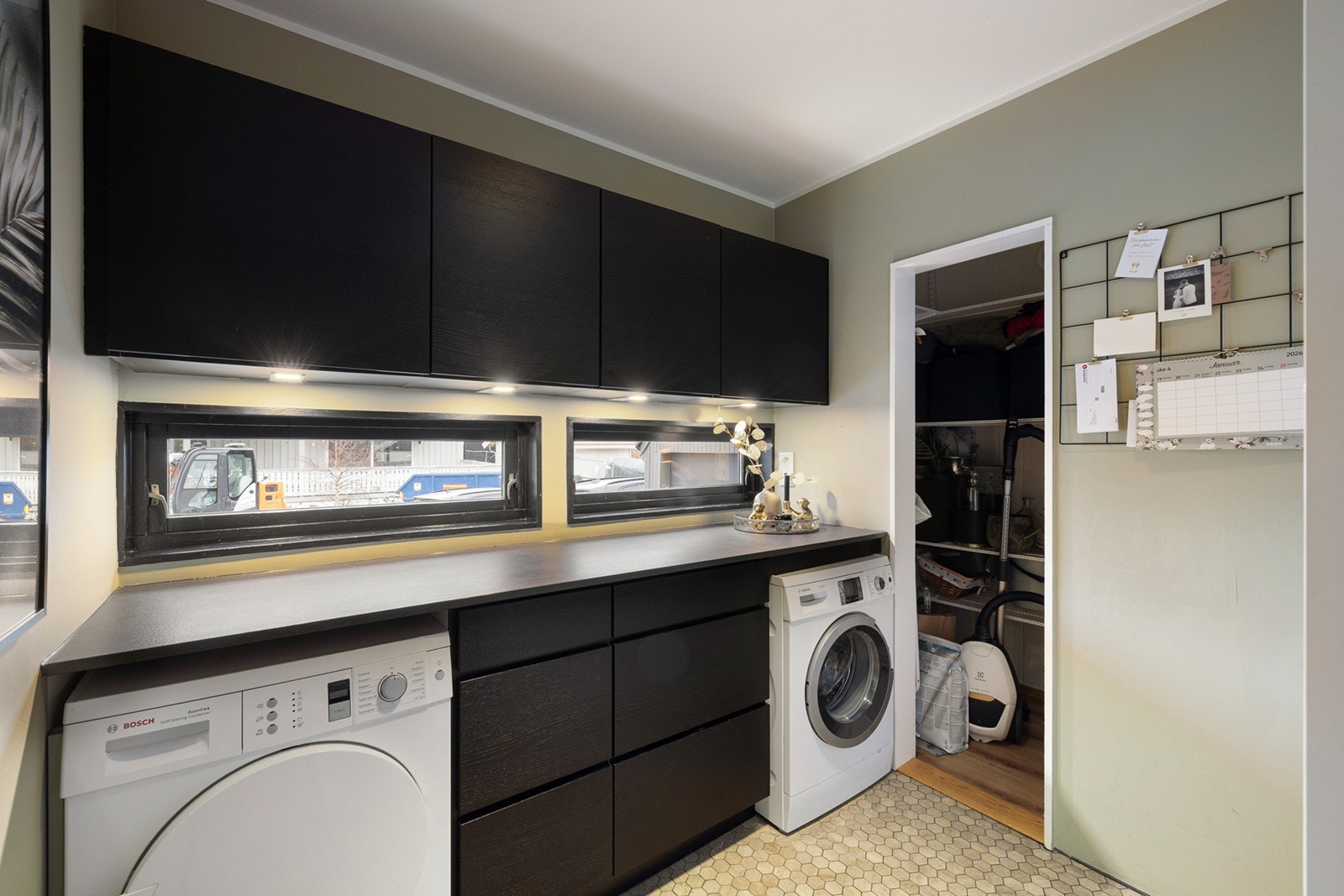 Praktisk og romslig vaskerom med god benkeplass og rikelig med oppbevaring i skap og skuffer. Det er opplegg for både vaskemaskin og tørketrommel, samt flislagt gulv med gulvvarme som gir ekstra komfort. Galleribilde