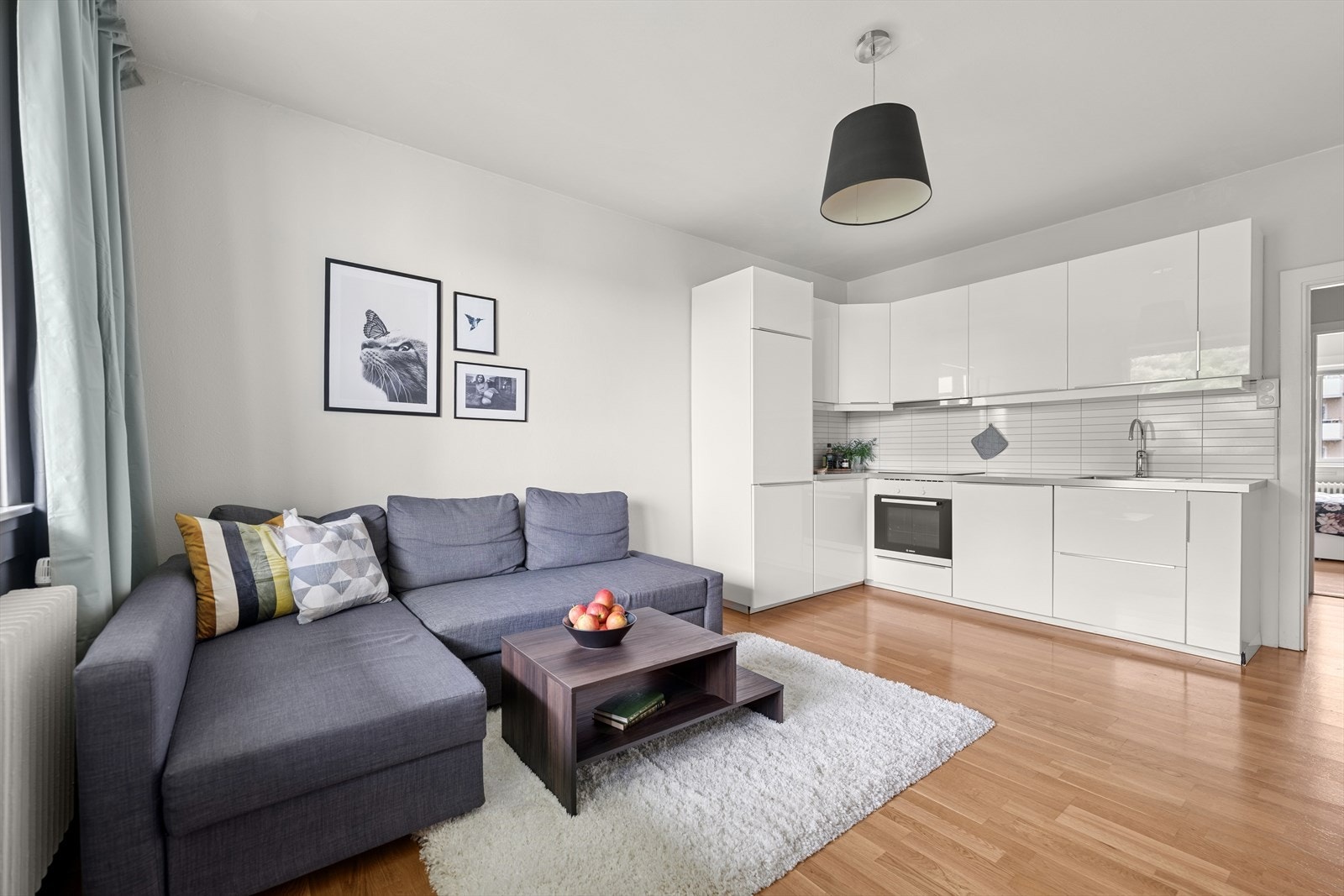 Det stilrene kjøkkenet fra 2016 har glatte, hvite fronter og laminatbenkeplater, noe som gir et rent uttrykk. Kjøkkenet er utformet i en praktisk vinkel, som gir rikelig med benkeplass og god lagringskapasitet i skap og skuffer. Galleribilde