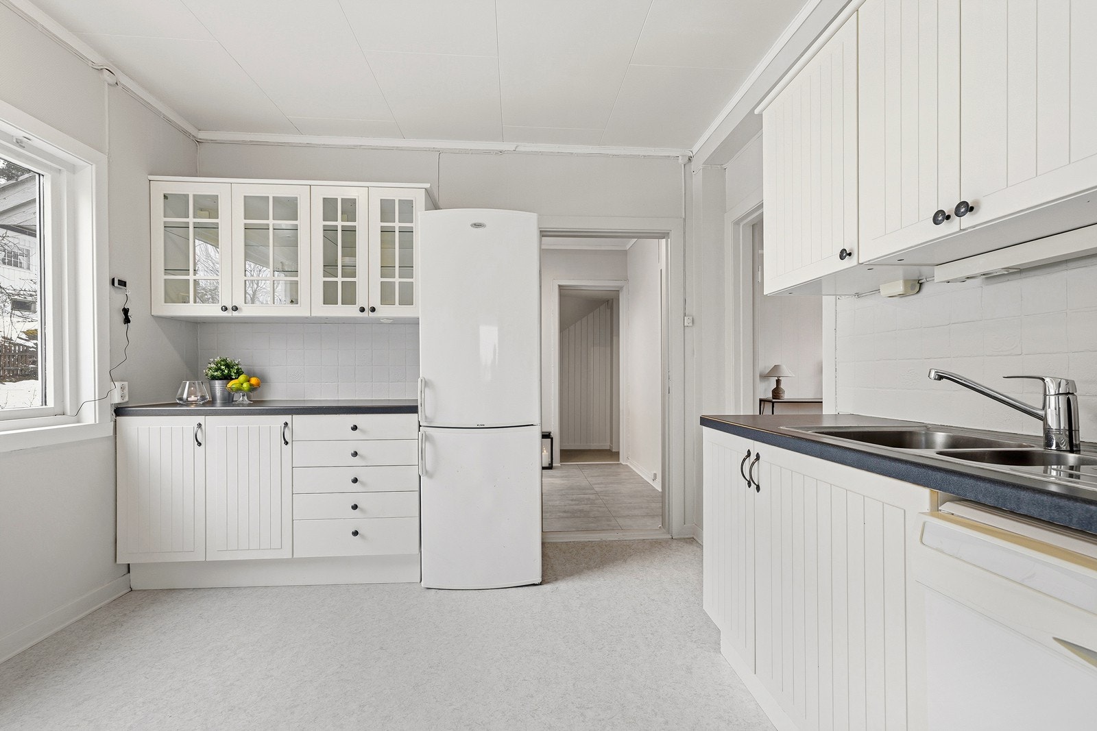 Kjøkkenet har behandlet innredning med profilerte, malte fronter. En del av overskapene har glass. Godt med skapplass over den den flissatte benken. Galleribilde