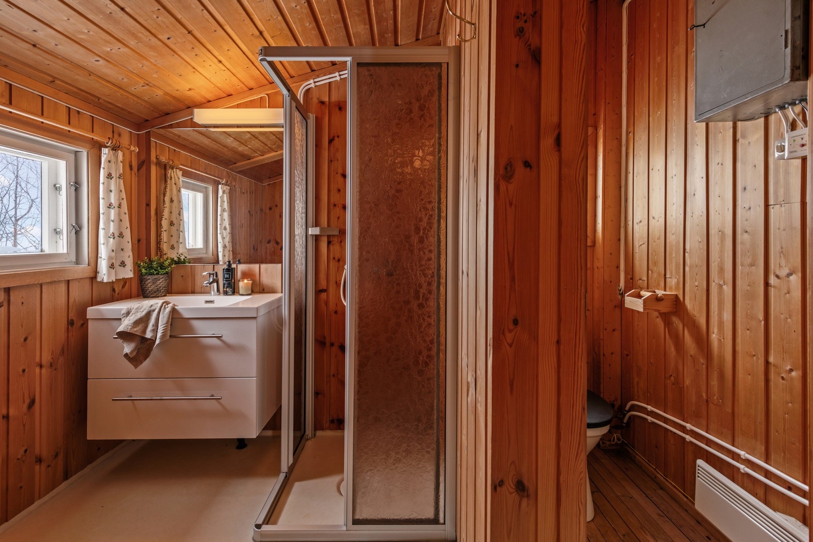 Badet har trepanel på vegger og tak, dusjkabinett, servant med skuffer og speil, samt vinduer som gir naturlig lys. Galleribilde