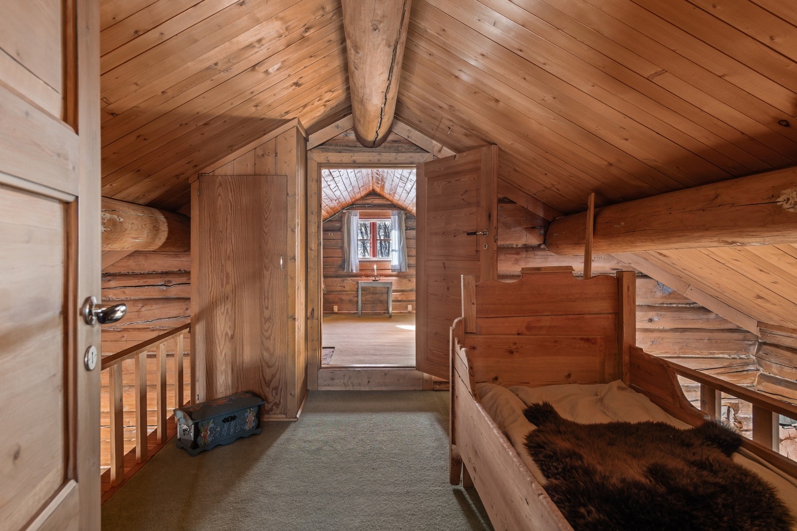 Hytta har en koselig hems med trepanel og åpen løsning mot et rom med vindu Galleribilde