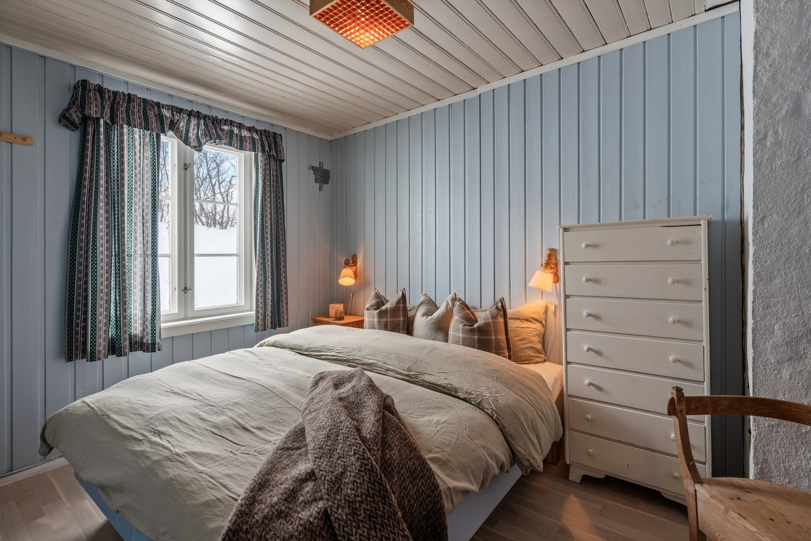 Koselig soverom med malte panelvegger og vindu som gir flott utsikt til naturen. Perfekt for avslapning og ro Galleribilde