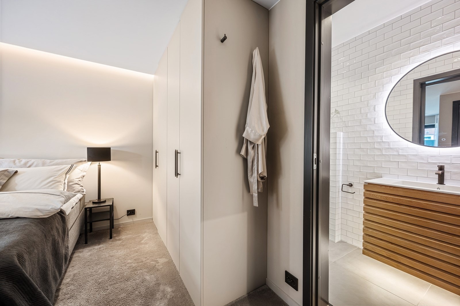 Soverommet har direkte adkomst til det stilrene badet. Badet er helfliset med varme i gulv. Rommet har vegghengt toalett, moderne baderomsinnredning, dusj og et stort speil med integrert lys. Galleribilde