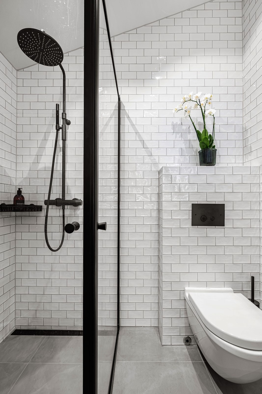 Vegghengt toalett, moderne baderomsinnredning, dusj og et stort speil med integrert lys. Rommet har balansert ventilasjon med avtrekk i himling og tilluft via spalte under dørblad. Galleribilde