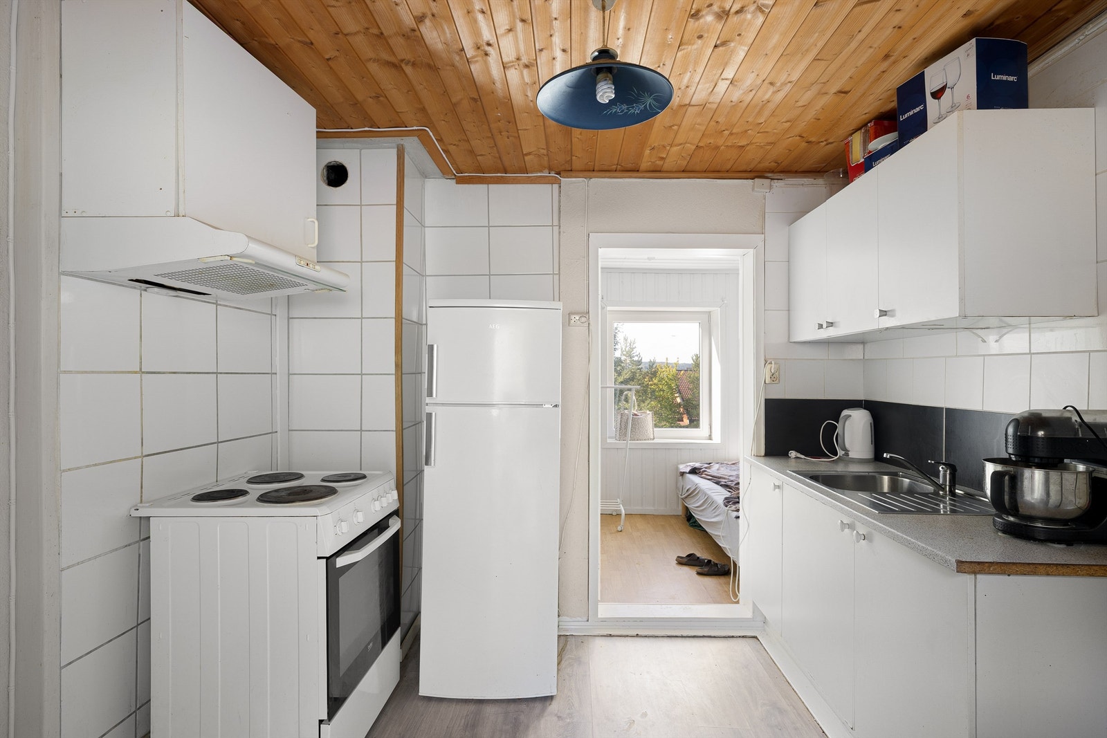 Kjøkken i leilighet #2, med tilstøtende soverom. Kjøkkeninnredningen har stor slitasjegrad. Galleribilde