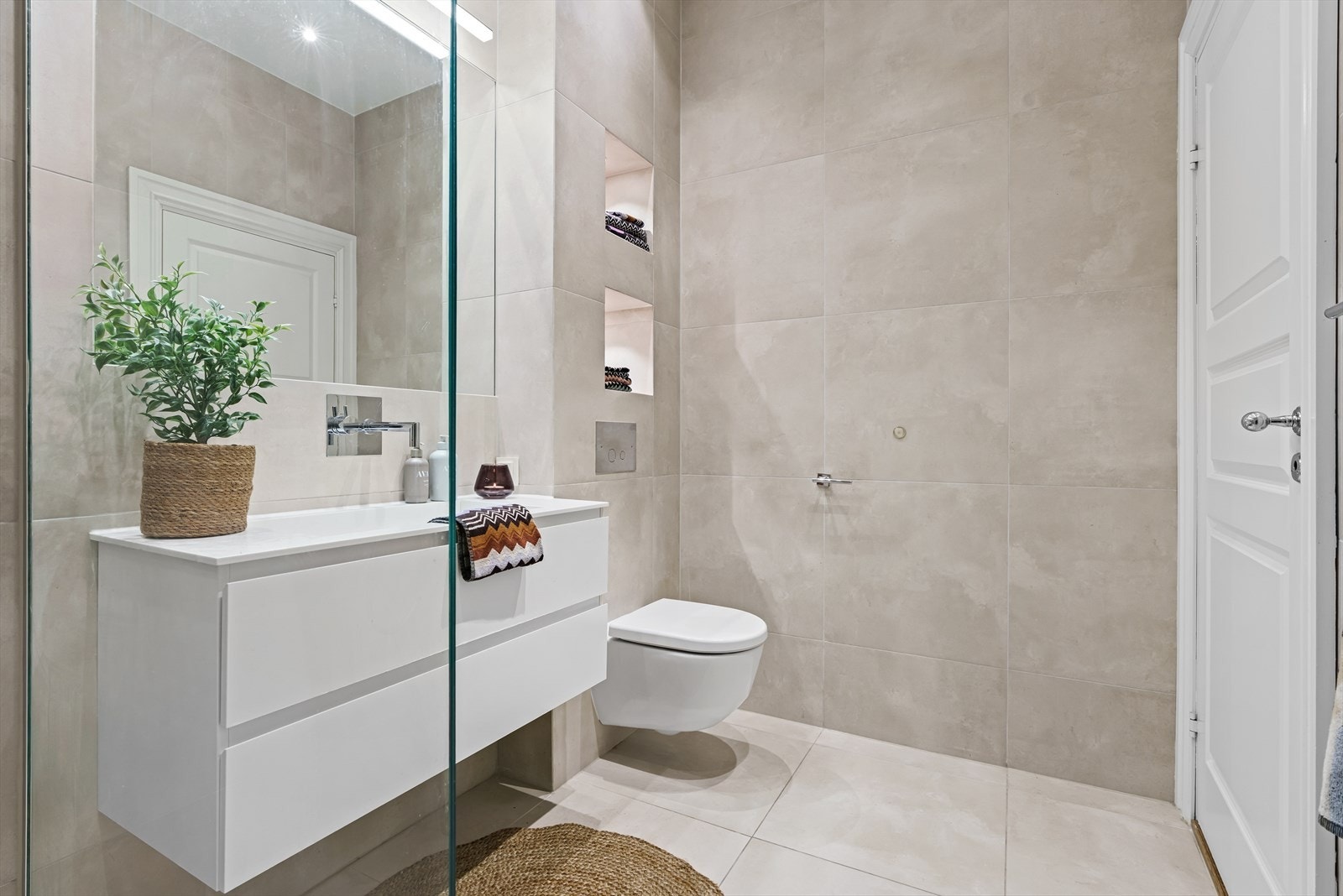 Rommet er innredet med veggfestet toalett, servant, innsmurt speil og dusj på gulv. Det er god plass til oppbevaring i benkeskap og innebygde hyller i veggen. Galleribilde