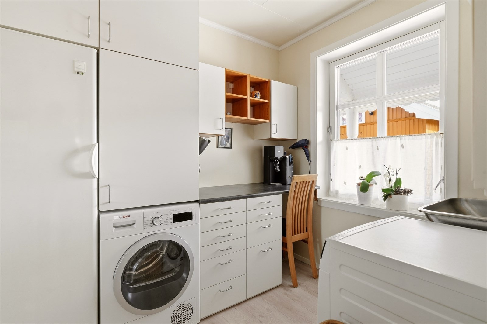 Praktisk vaskerom med skyllekar og opplegg for vaskemaskin. Overflatene består av takess i himlingen, malte plater på vegger og laminat på gulv. Galleribilde