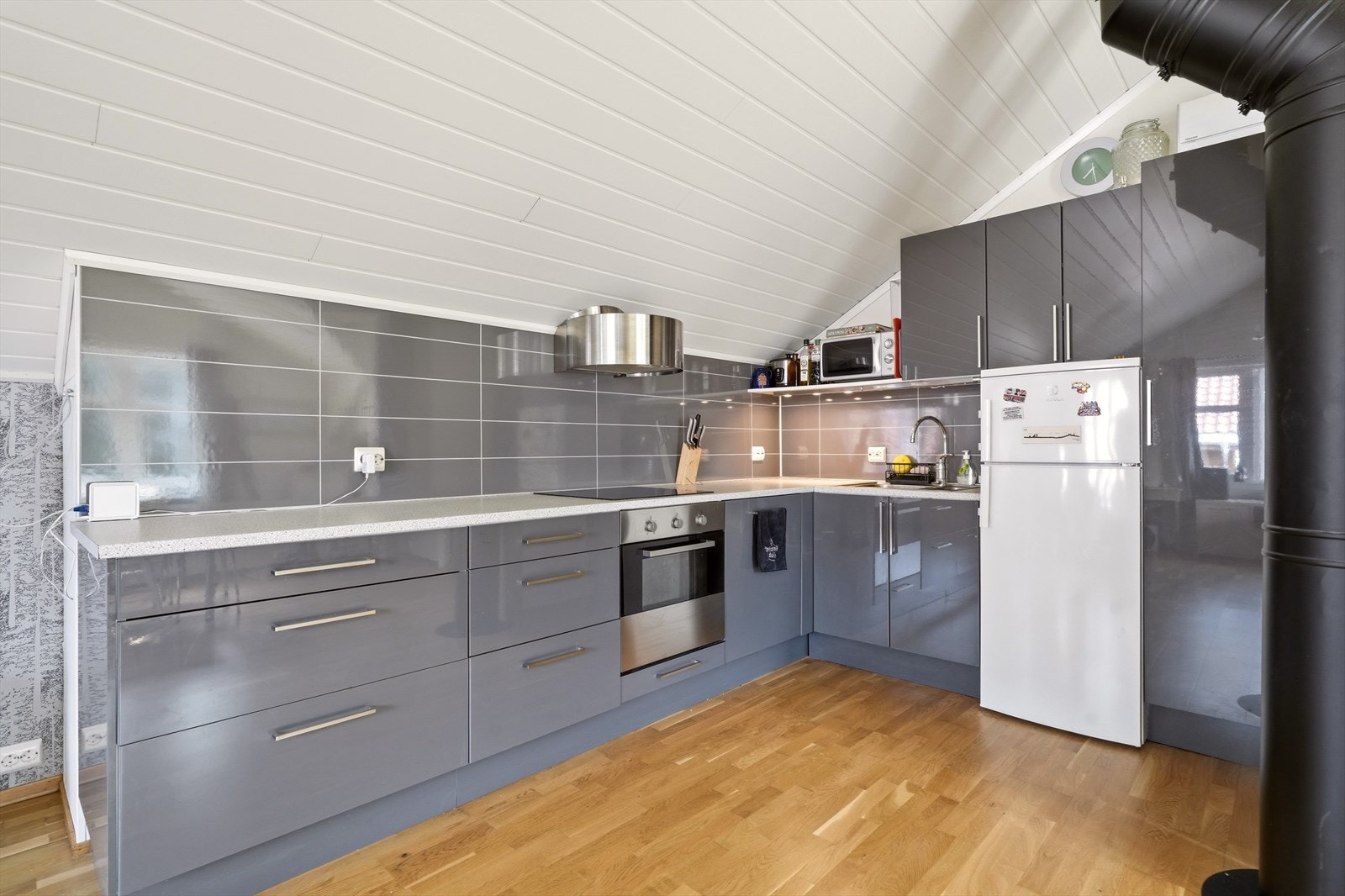 Innredet kjøkken har glatte fronter, laminert benkeplate, komfyrtopp, stekeovn, ventilator, oppvaskmaskin og kjøl/frys. Overflater består av MDF-panel i himling, panelplater på vegger og parkett på gulv - en lys og trivelig kjøkkenløsning. Galleribilde