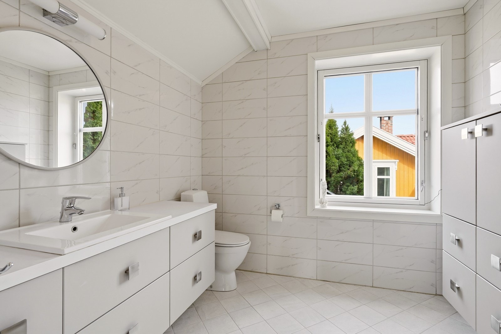 Romslig bad med flislagte gulv med varmekabler, flislagte vegger og malt himling. Rommet er innredet med servant i møbel, toalett og dusjhjørne - funksjonelt og praktisk. Galleribilde