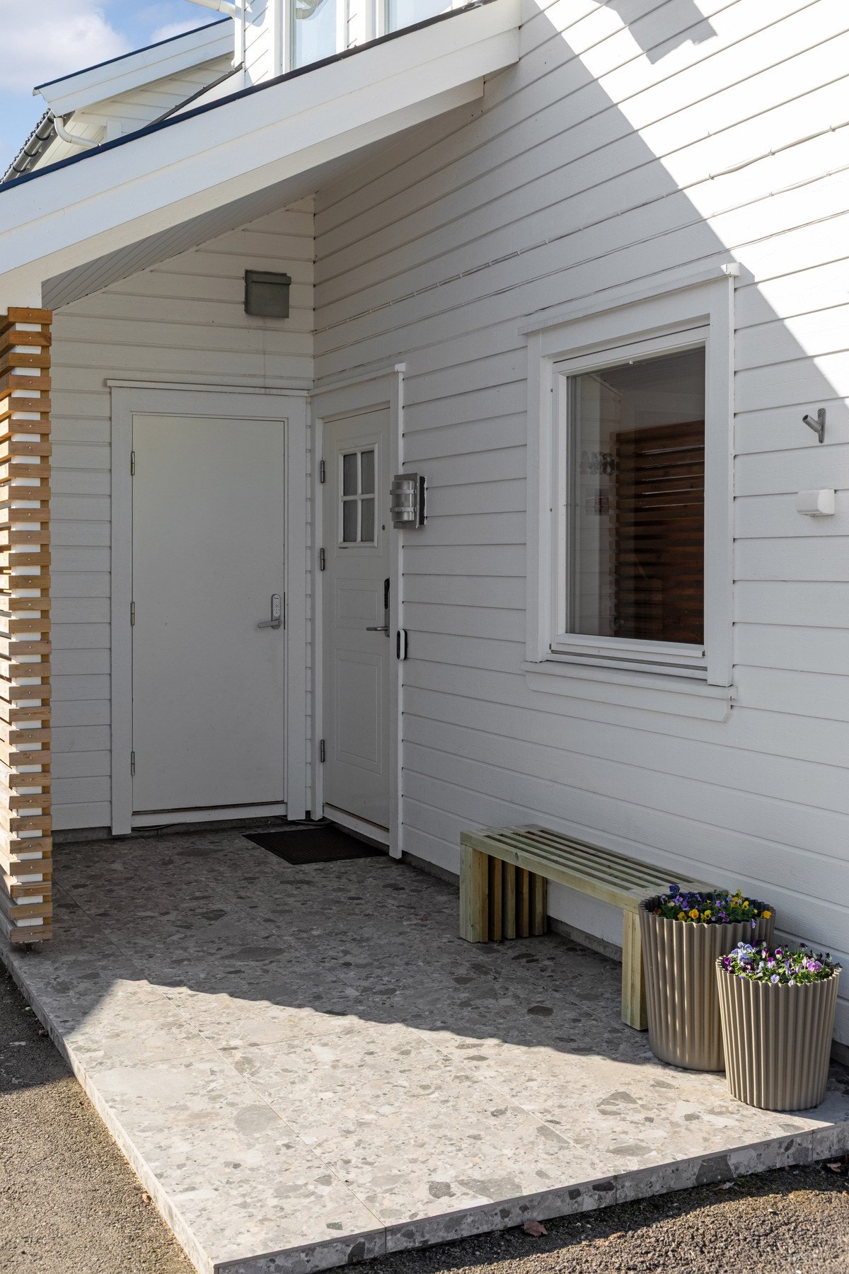 Ved inngangspartiet er gårdsplassen asfaltert, og boligen har en innbydende adkomstterrasse som ble flislagt i 2025, samt oppgradert med moderne spilevegg i 2024. Galleribilde