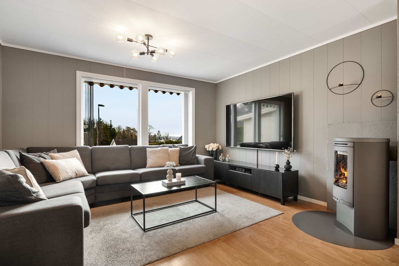 Stuen har store vindusflater og et dus, delikat fargevalg. Peisovn som skaper lun varme og en hyggelig atmosfære. Galleribilde