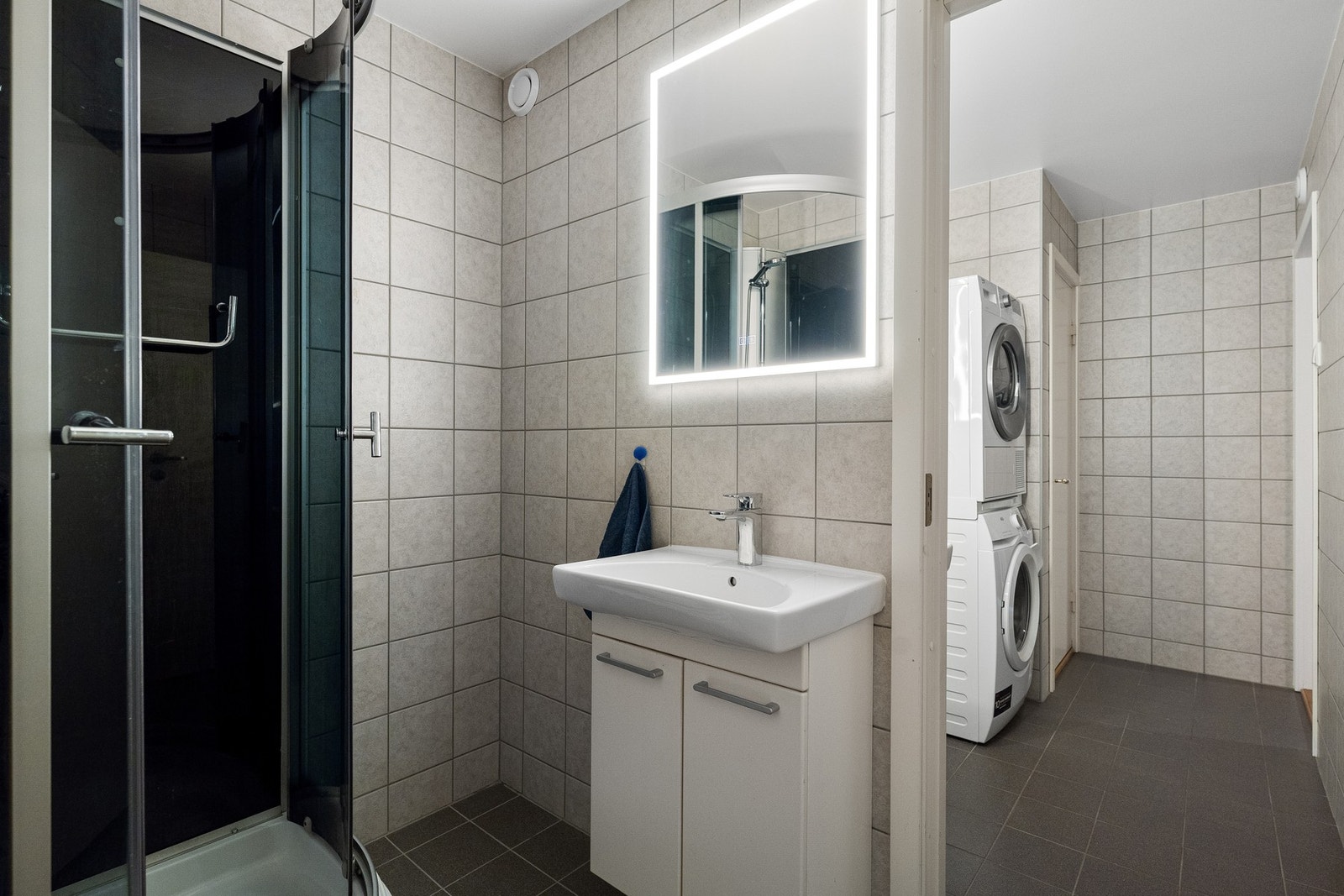 Badet er utstyrt med vegghengt servantinnredning med ovenpåliggende servant, speil med belysning og dusjkabinett. Galleribilde