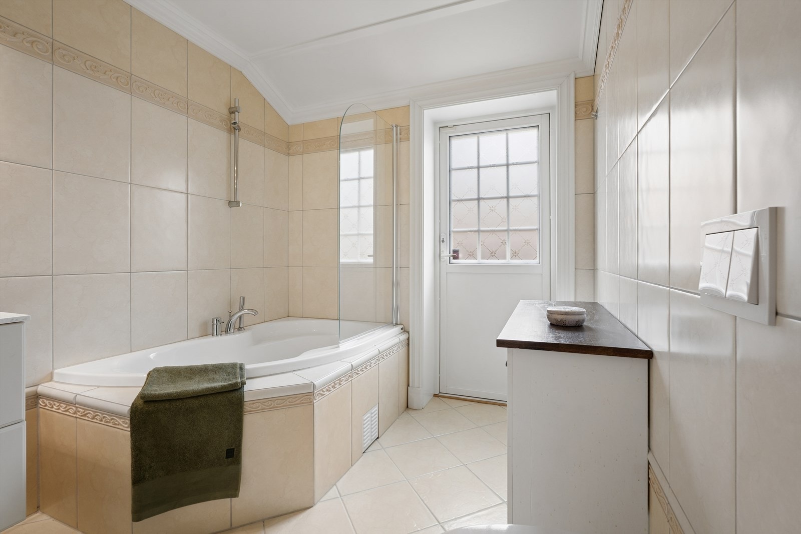 Sanitærutstyret omfatter en helstøpt servantplate, innfliset hjørnebadekar med glassvegg og dusjgarnityr, samt vegghengt toalett. Badet har balansert ventilasjon og varmekabler som gir ekstra komfort. Galleribilde