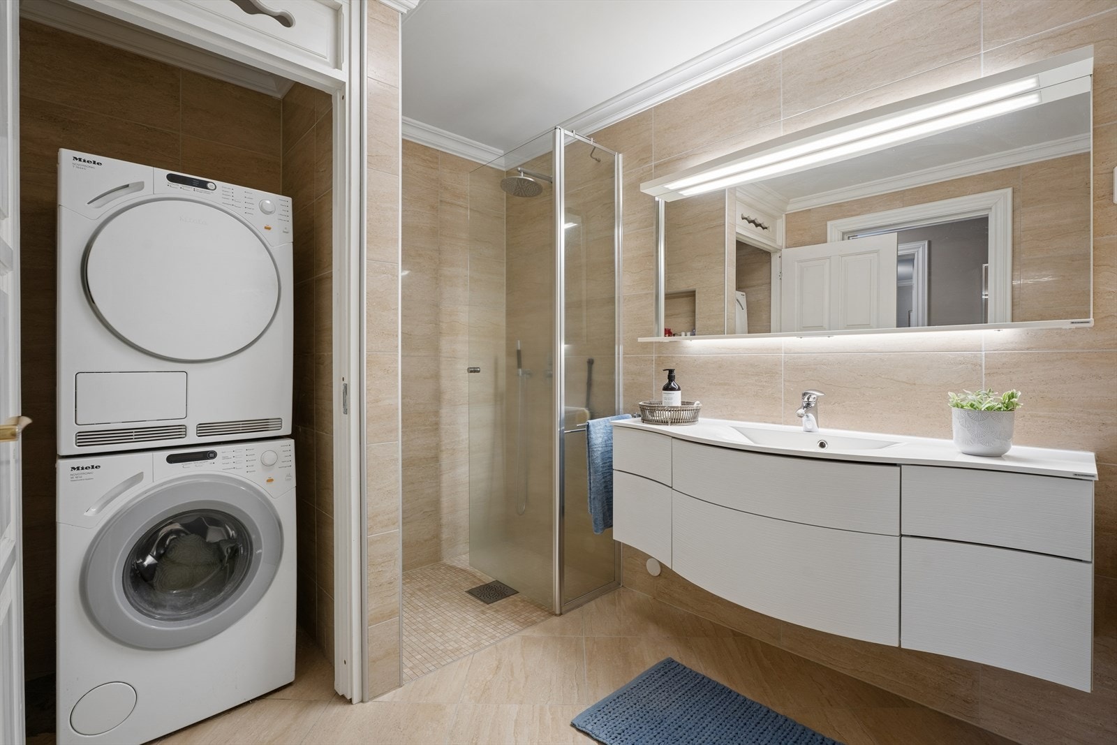 Innredningen består av vegghengt toalett, servant med servantskap, speil og dusjhjørne med glassvegg. I tillegg er det en praktisk nisje med opplegg for både vaskemaskin og tørketrommel. Galleribilde