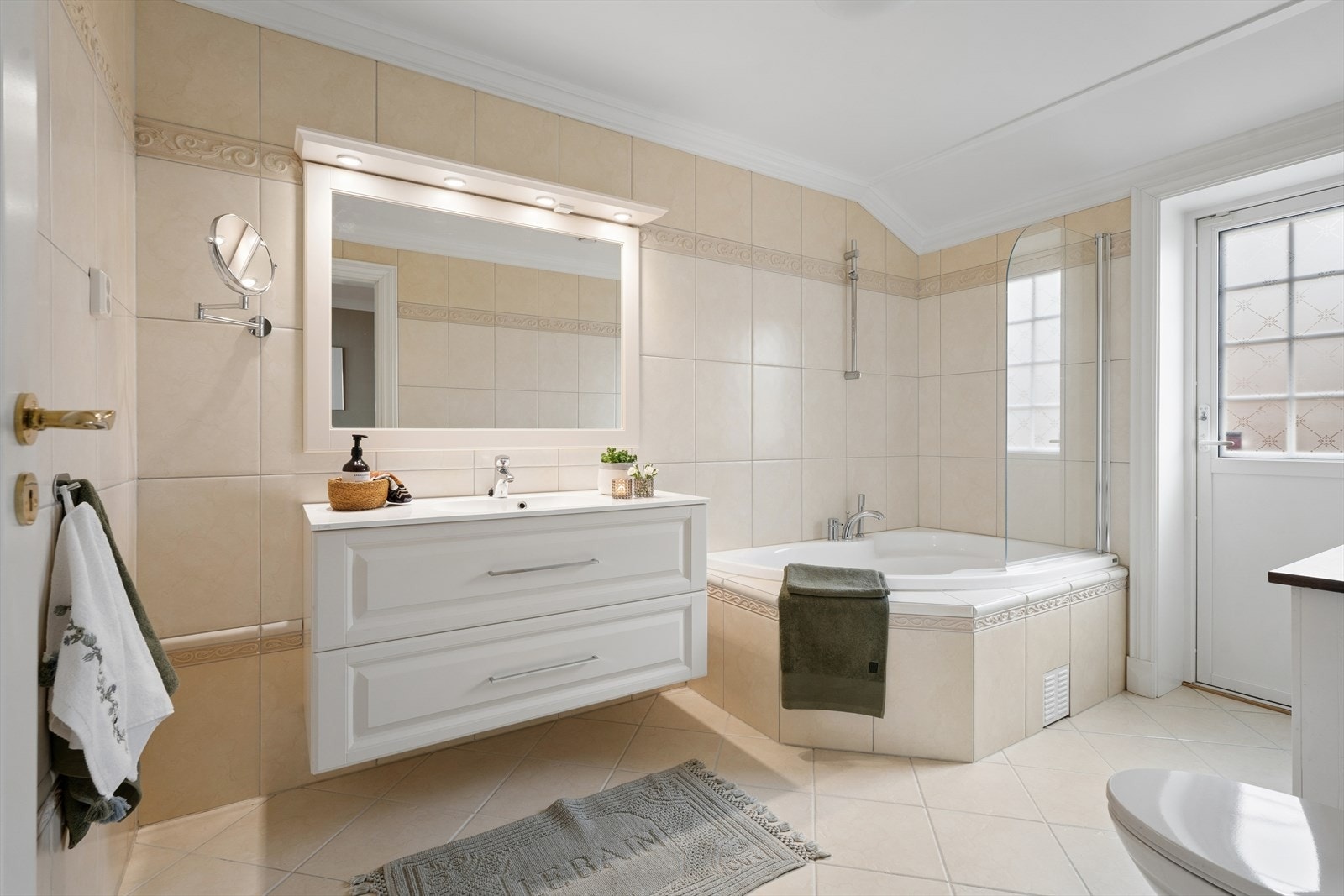 Hovedbadet ligger i 1. etasje. Badet fremstår delikat og innbydende med flislagte overflater i en elegant beigetone på både vegger og gulv. Galleribilde