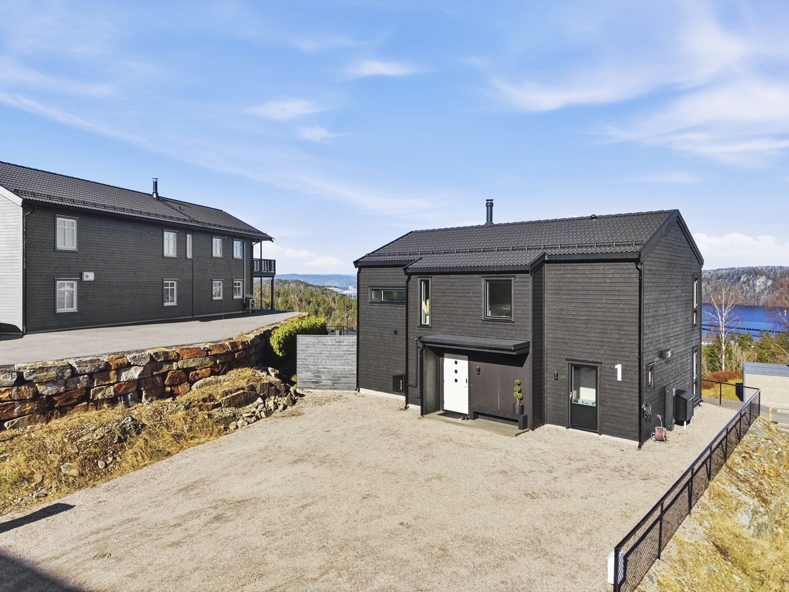 Romslig, gruset gårdsplass med elbillader. Tomten er i all hovedsak inngjerdet, både med gjerde og hekk Galleribilde