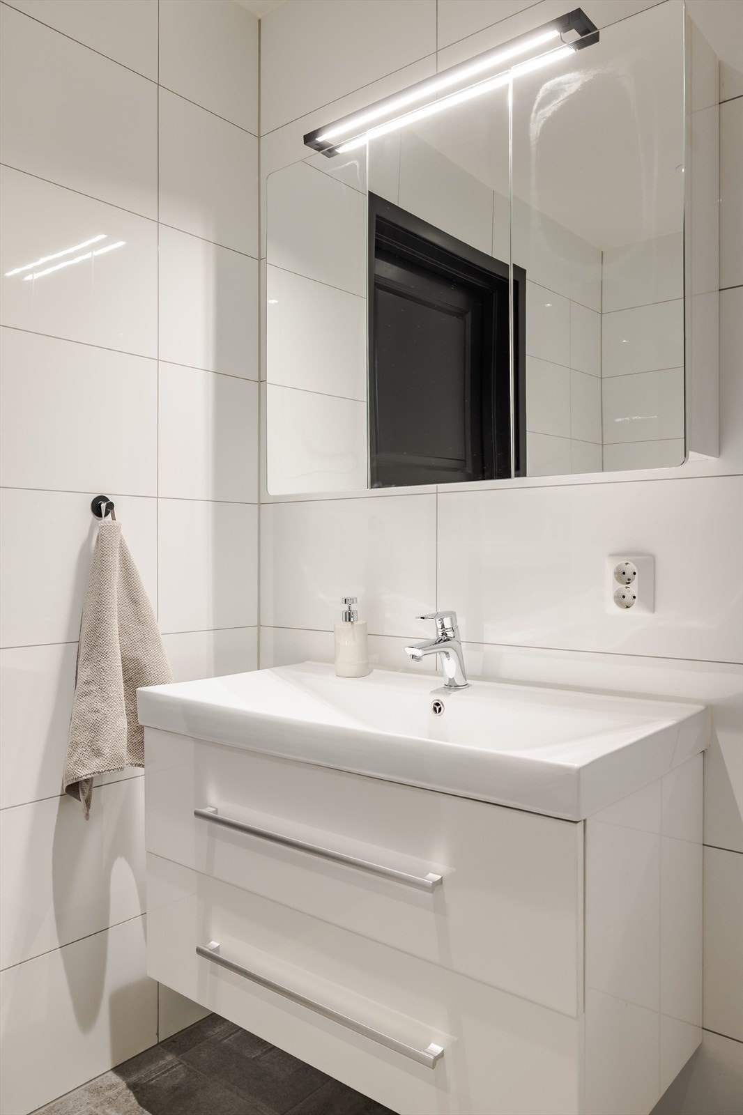 Moderne baderomsinnredning med skuffer og heldekkende servant, speilskap med belysning over. Galleribilde