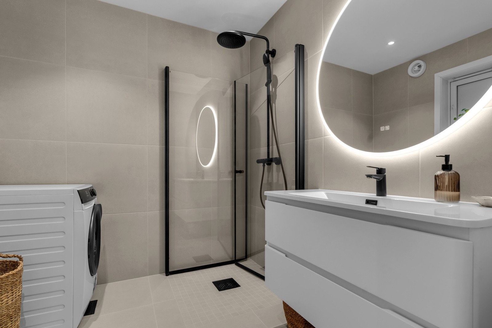 Badet er lekkert med lyse fliser på gulv og vegger, varmekabler i gulv, spotter i tak og opplegg til vaskemaskin. Galleribilde