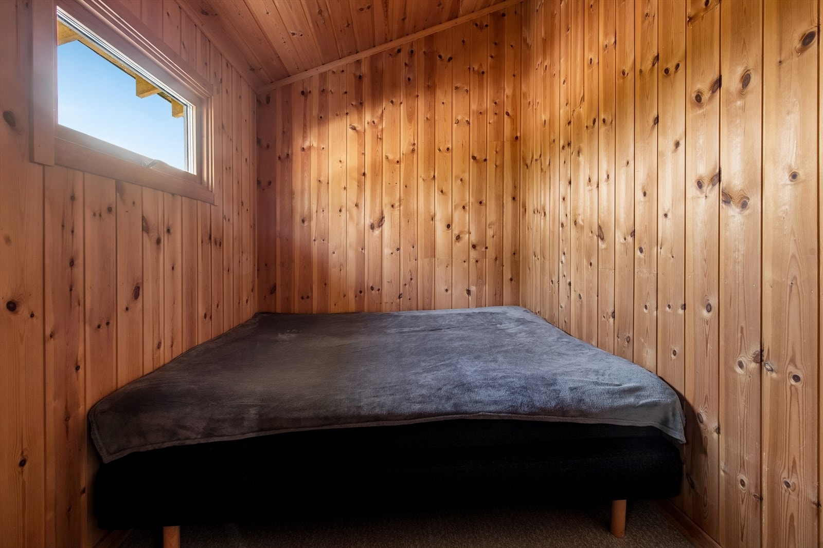 Et av de to soverommene i gjestehuset, med vegger og tak i trepanel. Galleribilde
