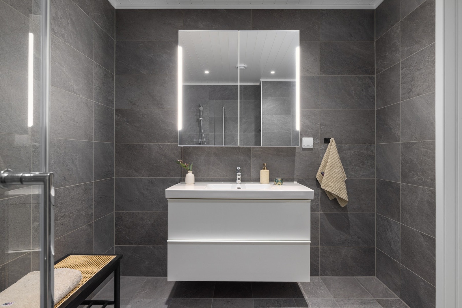 Badet er praktisk og gjennomført innredet med et stilrent dusjhjørne med glassvegger som gir en luftig følelse. Videre finner du et moderne toalett og en lekker servantinnredning Galleribilde