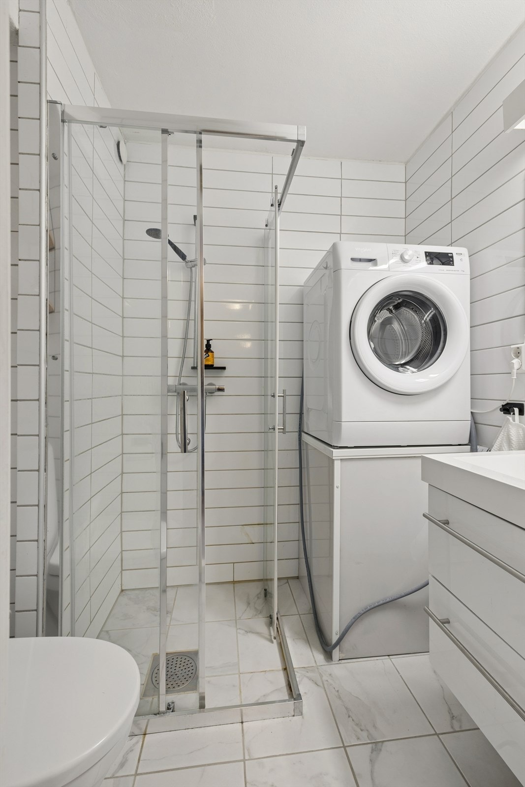 Lyst, flislagt bad med dusjhjørne, wc, servant med speil og opplegg for vaskemaskin. Galleribilde