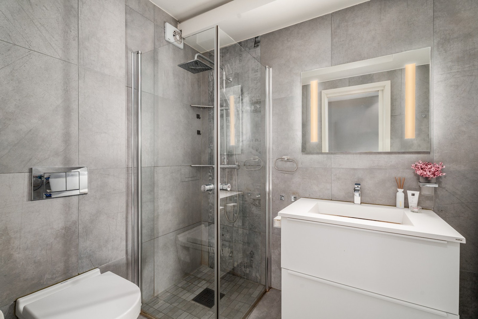 Badet er utstyrt med flislagt gulv, vegghengt toalett og regndusj. Galleribilde