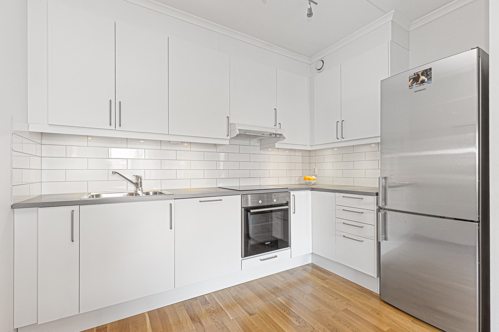 Lyse fronter i glatt utførelse. Fliser på vegg over laminat benkeplate, med gode arbeidsflater, nedfelt induksjonstopp og nedfelt oppvaskkum i rustfritt stål. Galleribilde