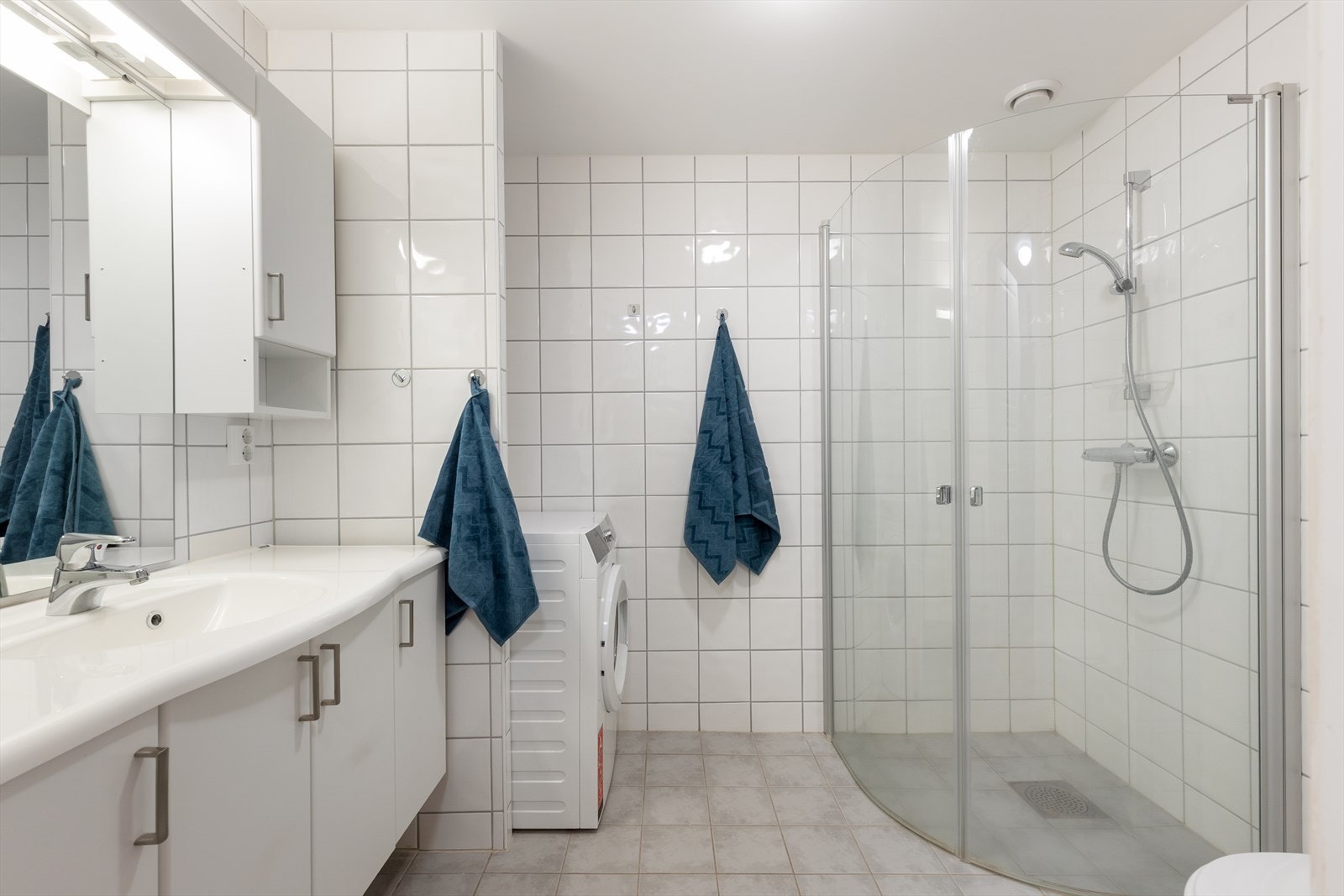 Badet har romslig og lyst servantskap, med heldekkende servantplate. På vegg over innredningen er det montert stort speil og overlys med el-stikk, samt praktiske sideskap med ytterligere oppbevaringsplass. Galleribilde