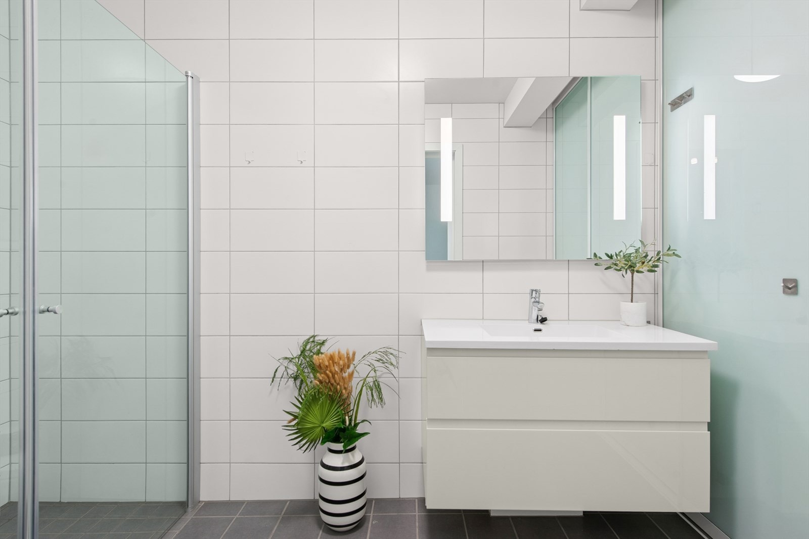 Dusjhjørne og romslig innredning. God belysning på baderommet. Bak skyvedørene til høyre kan man ha vaskemaskin og tørketrommel, og oppbevare klær og håndklær. Galleribilde