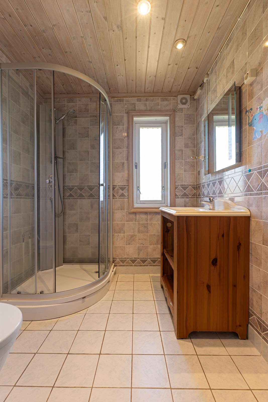 Lunt og koselig bad med flislagt gulv og baderomsplater på veggene. Badet er innredet med servantskap, dusjkabinett og toalett.
Down-light belysning i tak. Galleribilde