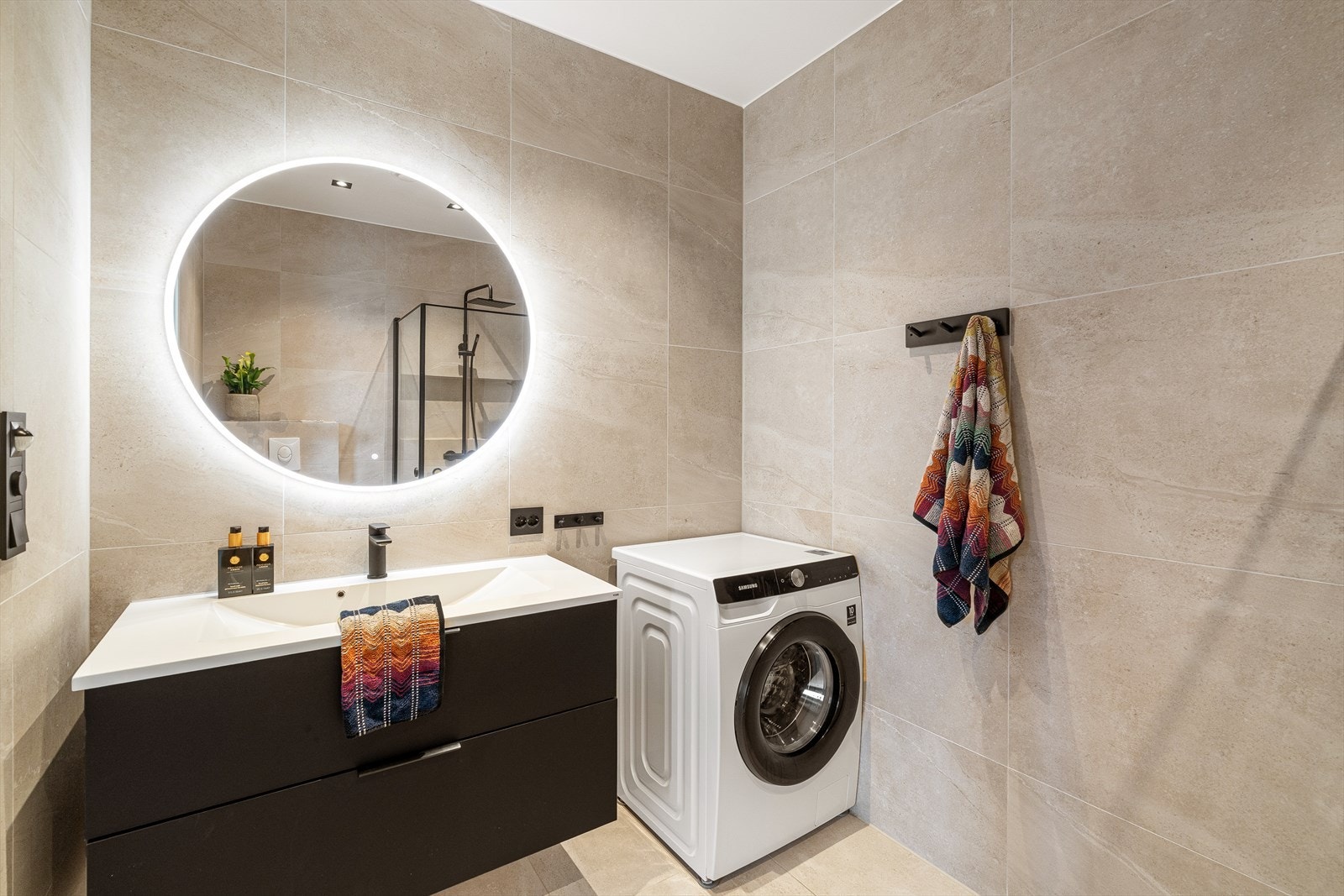 Badet er utstyrt med servant, vegghengt toalett og dusjhjørne. Baderomsinnredning med sorte fronter Galleribilde