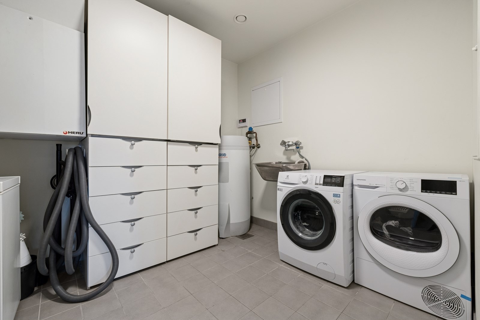 Vaskerom/teknisk rom med servant og opplegg for vaskemaskin, varmtvannstank, balansert ventilasjon og rørfordelerskap.. Fliser på gulv med elektriske varmekabler. Galleribilde