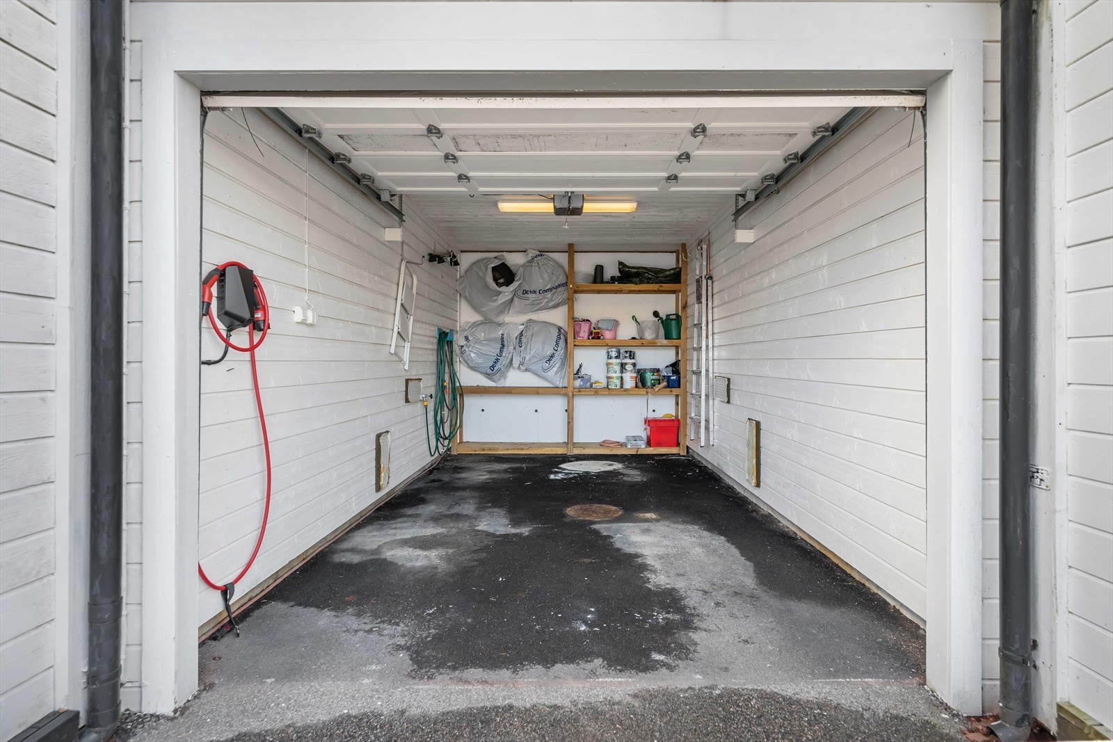 En praktisk garasje med lagringsplass i enden og asfaltert dekke. Det er også installert en lader for elektrisk bil. Galleribilde
