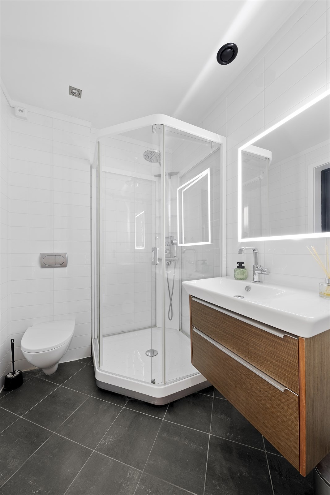 Badet i tilknytning til soverommet har flislagte overflater i nøytrale fargetoner - Her finner du vegghengt toalett, dusjkabinett og baderomsinnredning Galleribilde