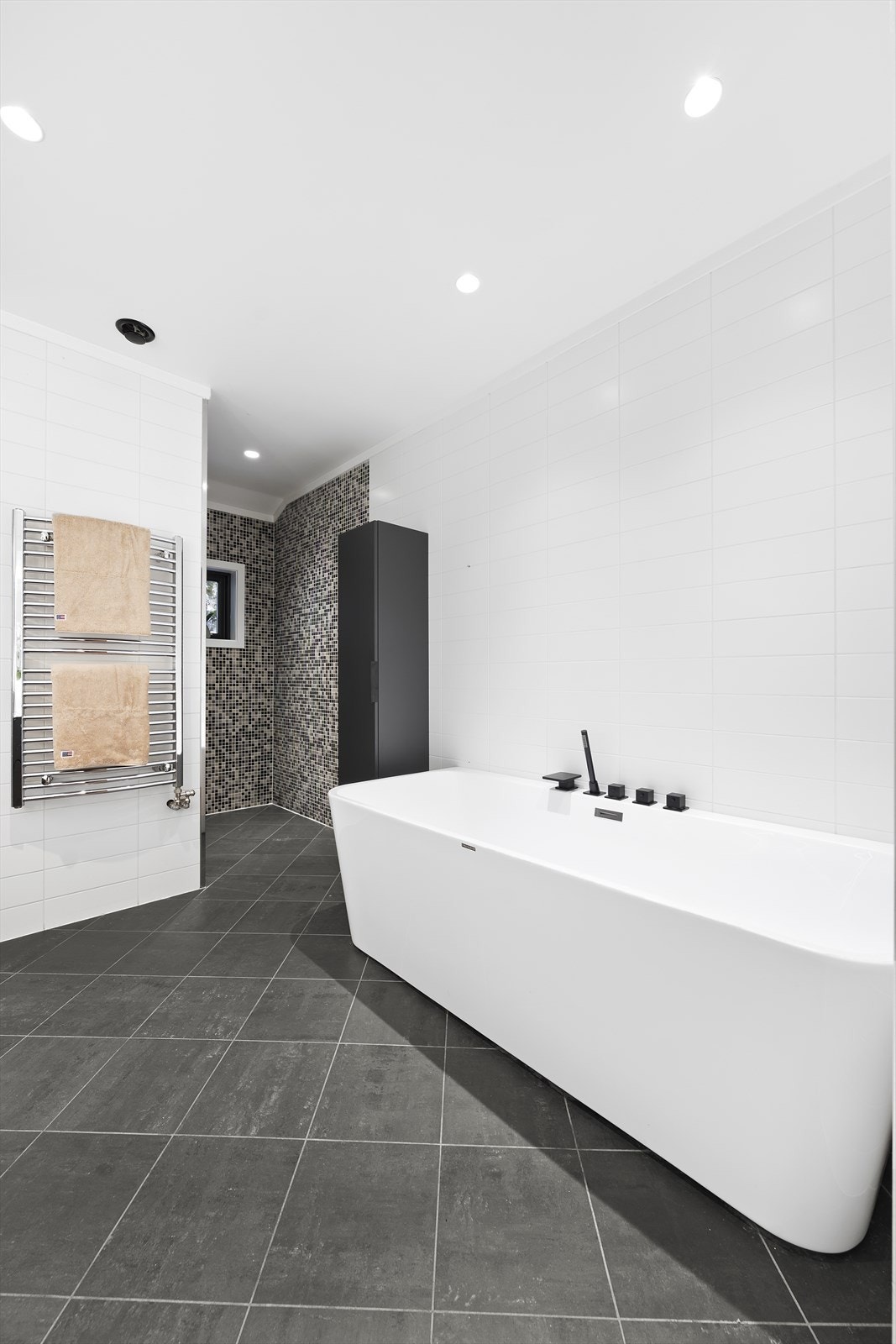 Rommet er utstyrt med badekar, dusjnisje, håndkletørker og baderomsinnredning i sort utførelse Galleribilde