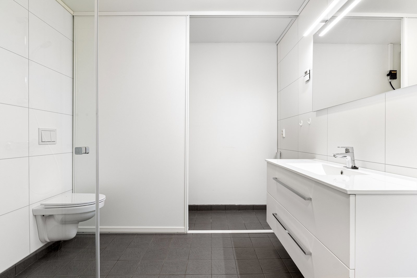 - Lyst og stort baderom som er utstyrt med vegghengt toalett, dusjhjørne, opplegg for vaskemaskin og servantinnredning - Galleribilde