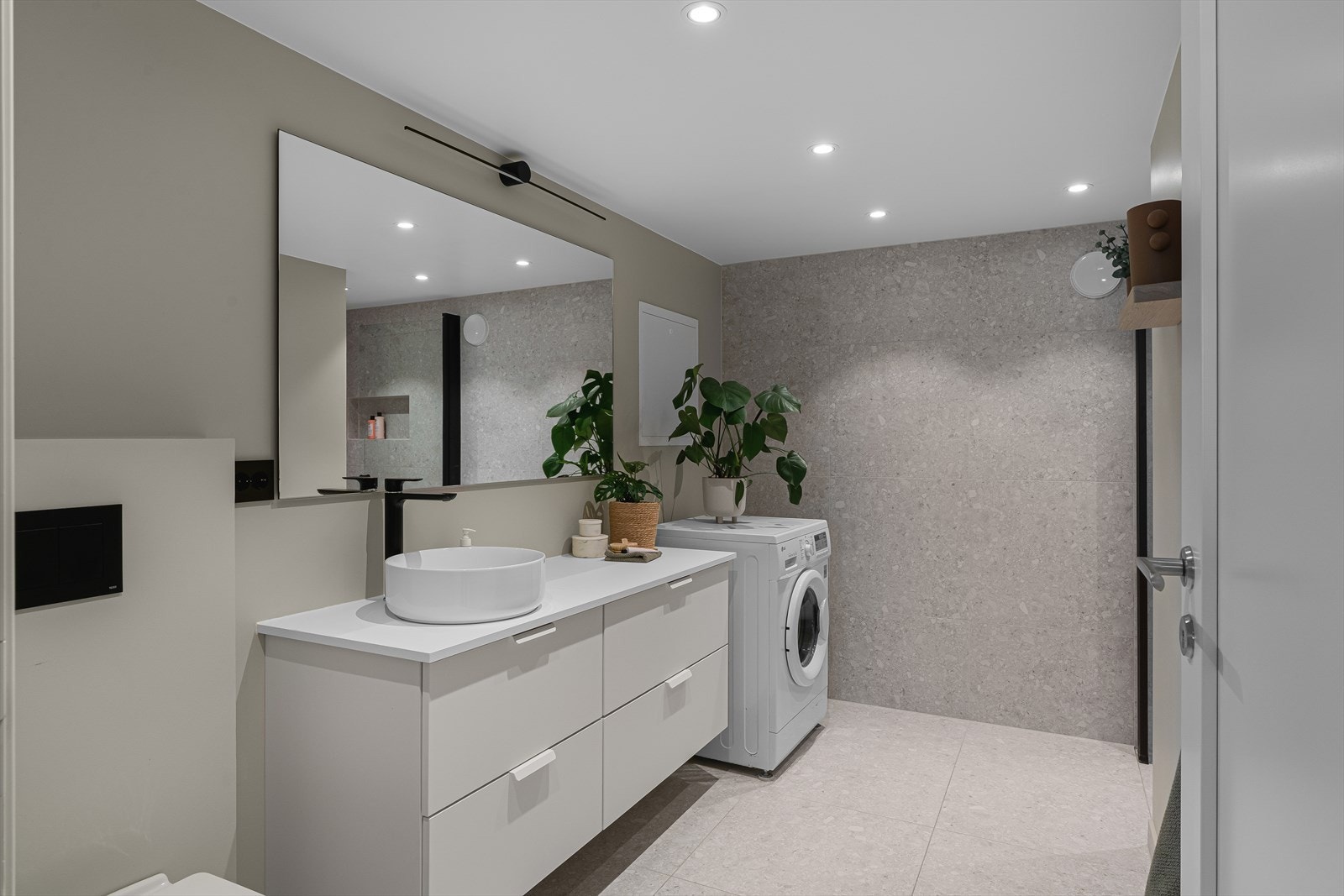 Lekkert kombinert baderom og vaskerom fra 2021 med store fliser på gulv og gulvvarme Galleribilde