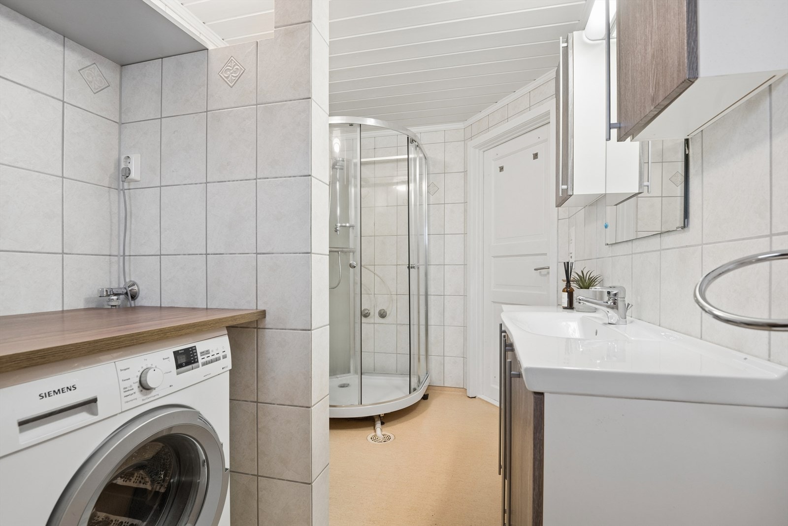 badet har gulvbelegg, fliser på vegg og panel i himling. Innredningen består av opplegg til vaskemaskin, servant, dusjkabinett og vegghengt toelaett. Galleribilde