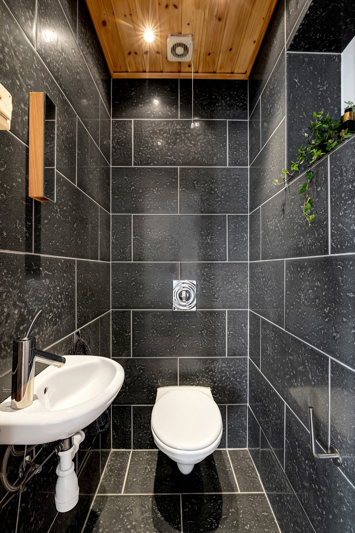 Separat toalettrom med flislagt gulv, servant og vegghengt toalett med innebygget sisterne - en praktisk løsning i hverdagen. Galleribilde