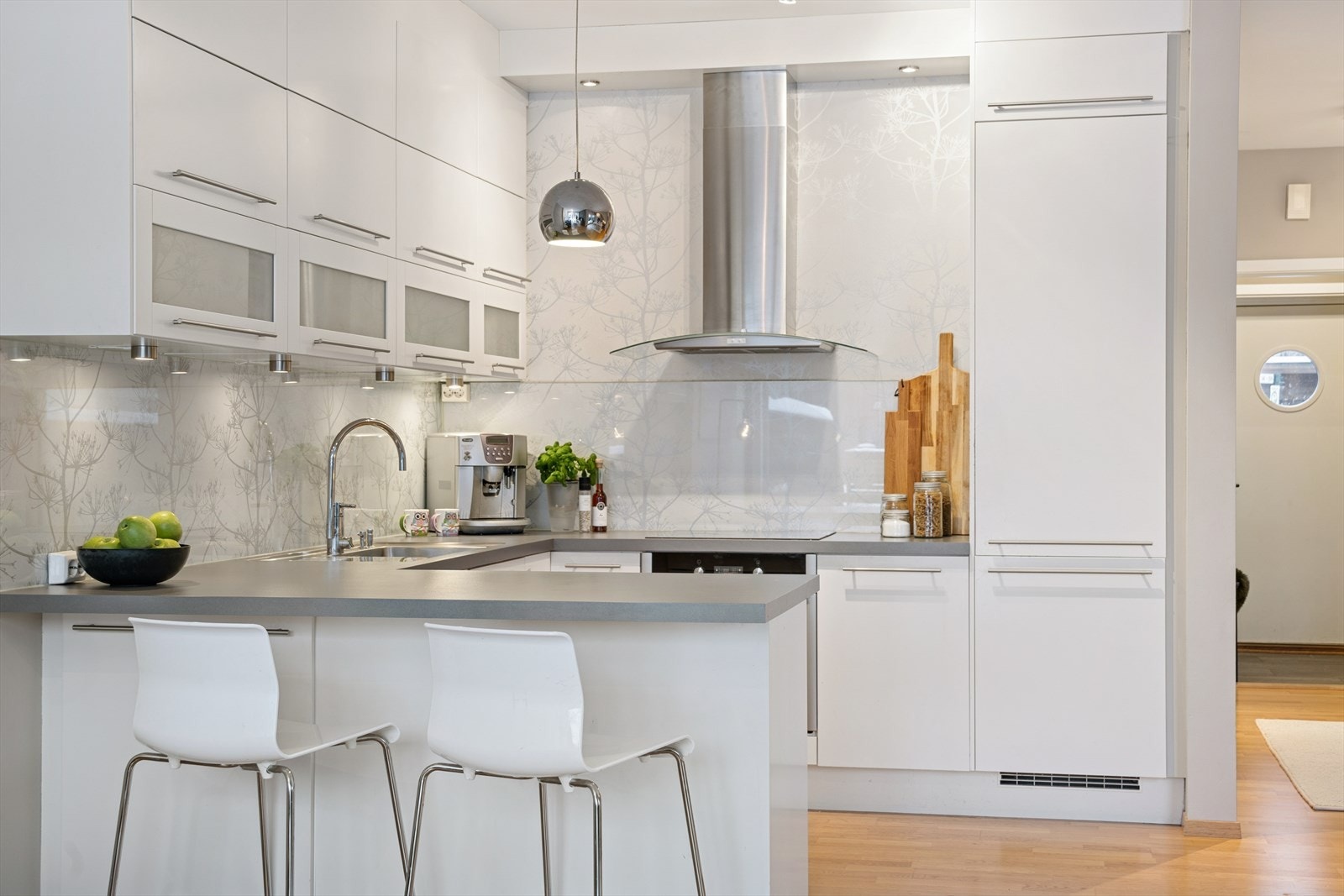 En praktisk halvøy strekker seg ut fra veggen og fungerer både som ekstra arbeidsflate og som en sosial sone i rommet, med plass til to barstoler - perfekt for uformelle måltider, morgenkaffen eller som et naturlig samlingspunkt når gjester er på besøk. Galleribilde